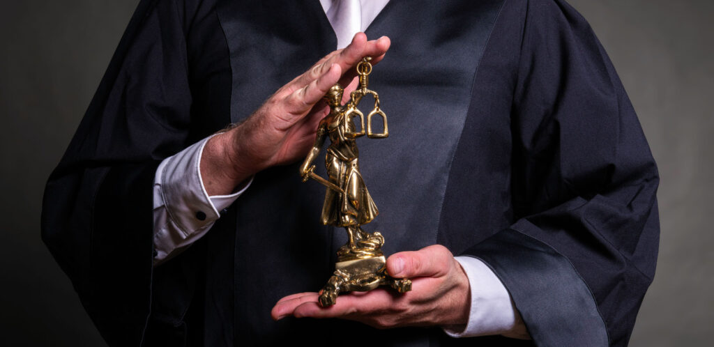 Ein Richter hat eine goldene Justitia-Statur in seiner Hand.