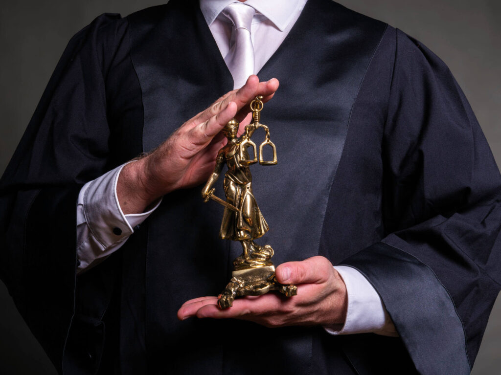 Ein Richter hält eine goldene Justitia-Statur in der Hand.